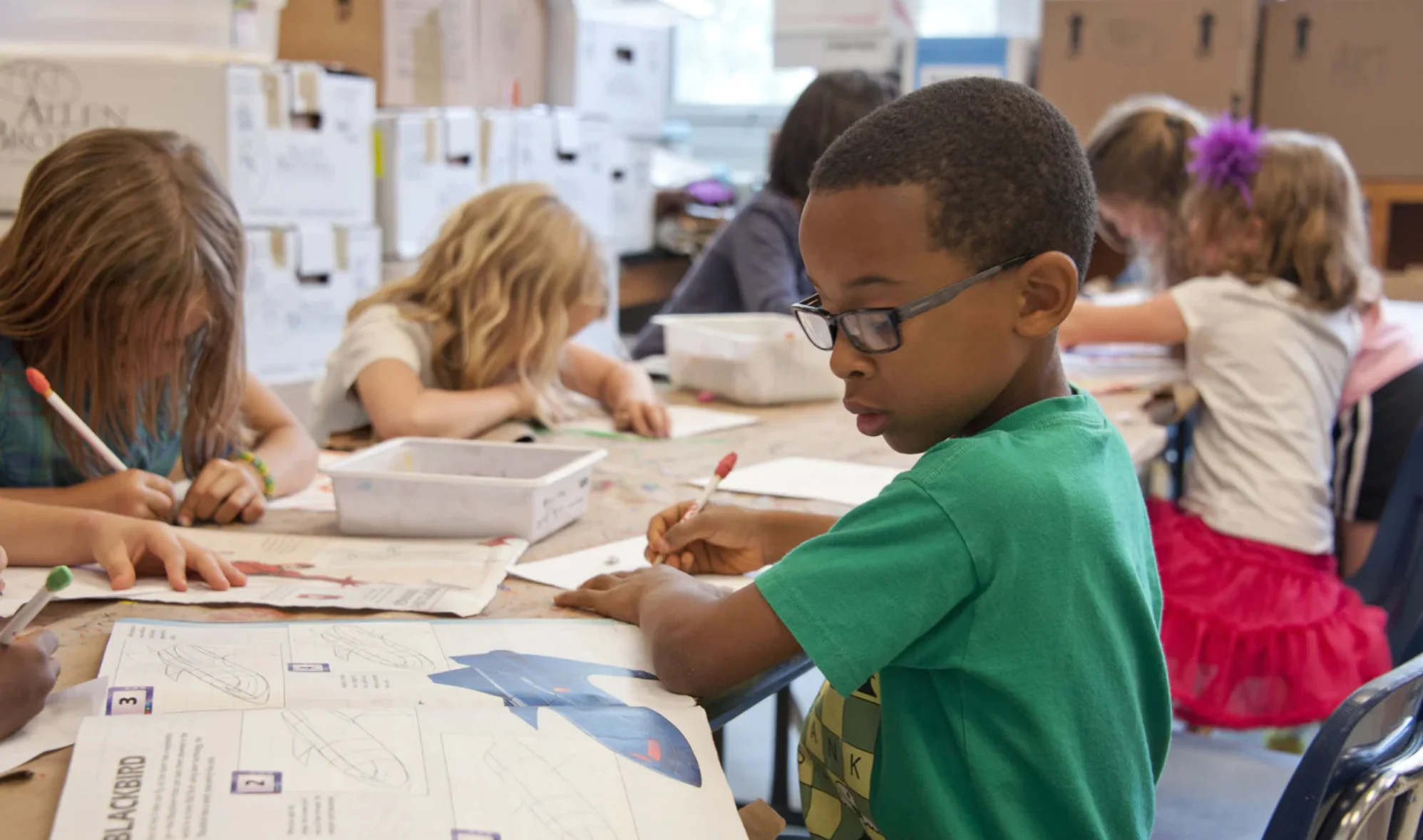 A boy is writing on paper while sitting at a table.