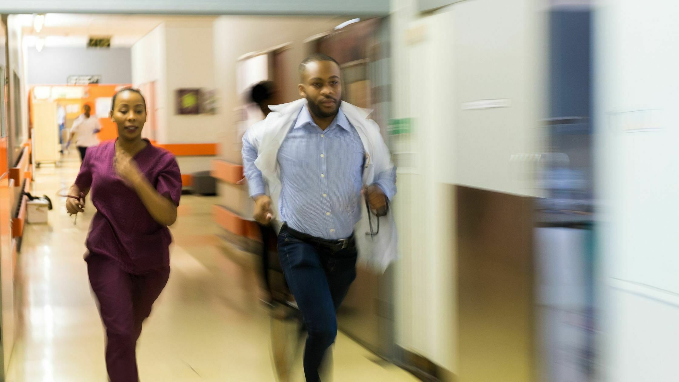 A man in blue shirt and white jacket running through hallway.